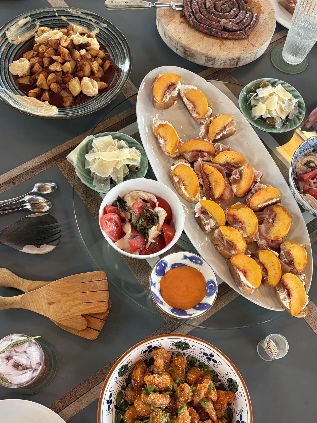 A table of peach crostini, potatoes, sausage, tomatoes, and fried chicken